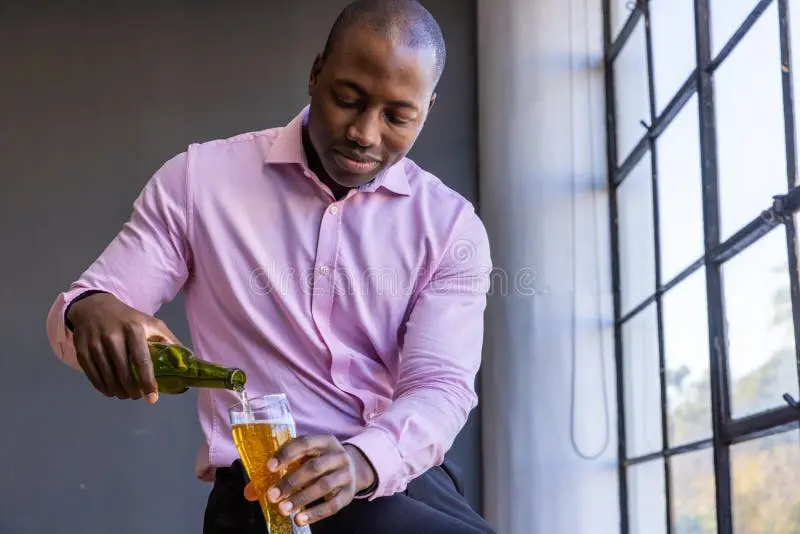 african-american-man-shirt-pouring-beer-green-bottle-pilsner-glass-loft-window-elegant-casual...webp